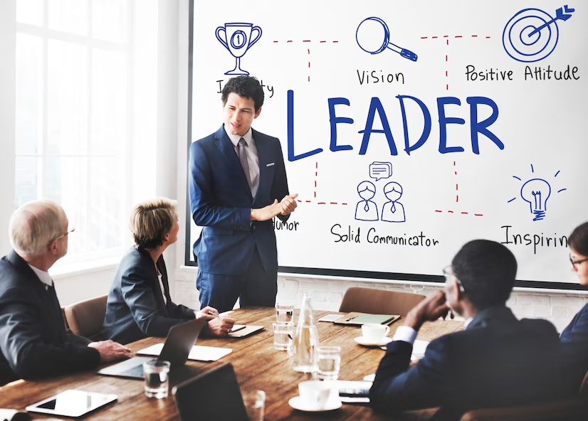 Man speaking to professionals in conference room with 'leadership' on whiteboard