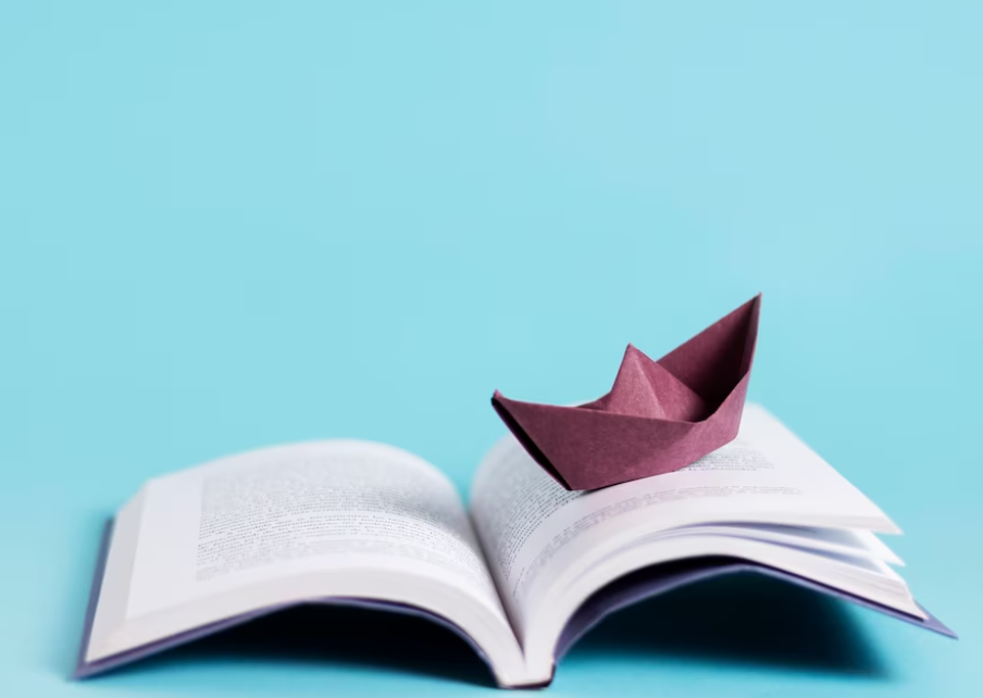 opened book and paper boat on it with blue background
