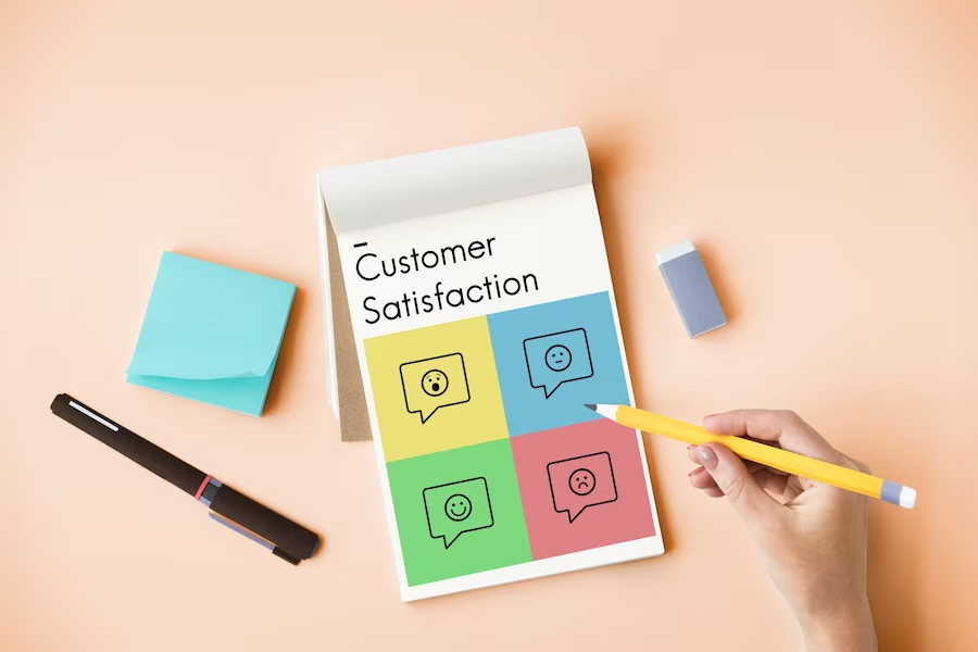 Hand holding a pencil and notepad on a table, with customer feedback icon and text 'Customer Satisfaction'